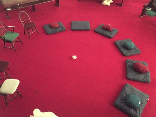 A circle of pillows on red carpet, prepared for meditation